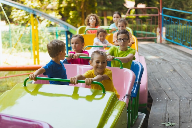 As crianças felizes em uma montanha-russa no parque de diversões