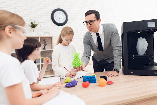 As crianças imprimem artigos diferentes na impressora 3d com um professor.