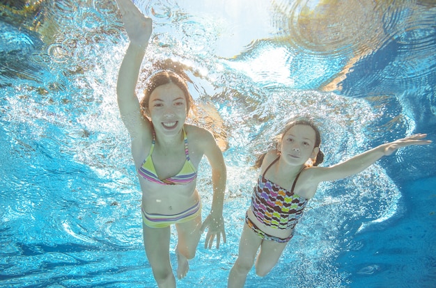 As crianças nadam debaixo d'água na piscina, felizes meninas ativas se divertem debaixo d'água, crianças fitness e esporte em férias em família ativas