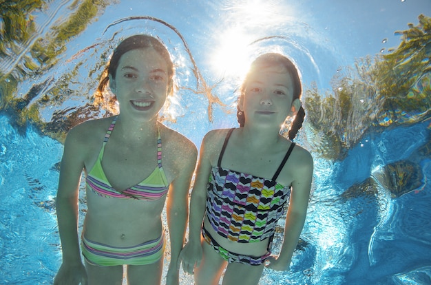 As crianças nadam debaixo d'água na piscina, felizes meninas ativas se divertem debaixo d'água, crianças fitness e esporte em férias em família ativas