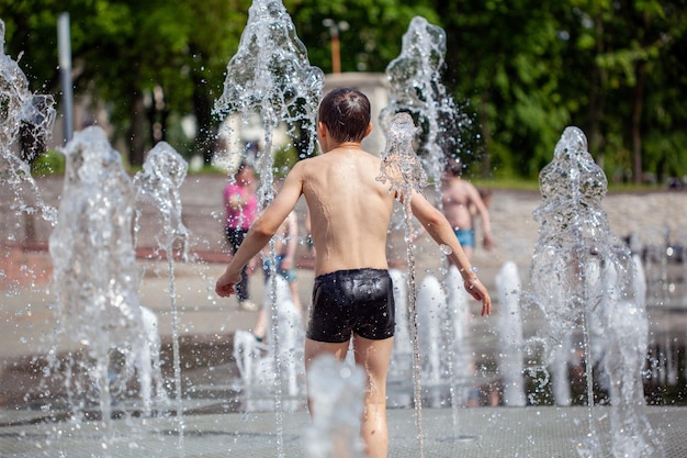 As crianças pequenas desconhecidas do tempo quente do verão banham-se na fonte da cidade no parque