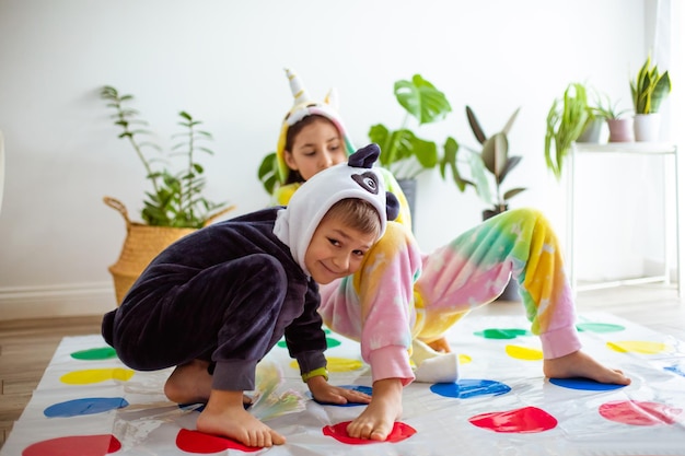 As crianças vestidas de kigurumi animal sentadas no chão da sala As crianças de pijama brincam de twister