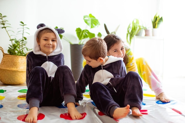 As crianças vestidas de kigurumi animal sentadas no chão da sala as crianças de pijama brincam de twister