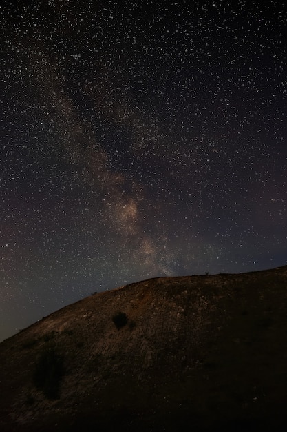 As estrelas da Via Láctea no céu noturno sobre uma paisagem montanhosa