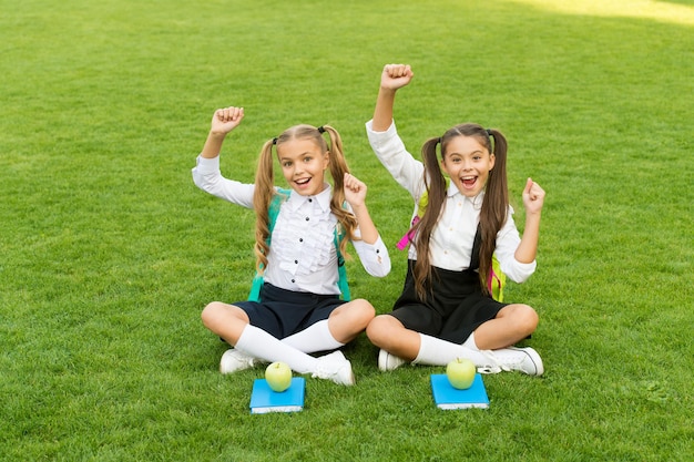 As férias começaram. Crianças felizes comemoram feriados ao ar livre. As meninas sentam-se na grama verde. Férias escolares. Férias e férias de verão. Lazer e tempo livre. A escola acabou.