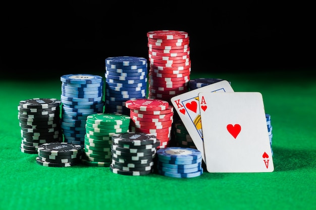 As fichas de pôquer são empilhadas com duas cartas rei e ACE. Sobre uma superfície verde.