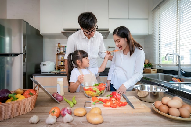 As filhas asiáticas que dão salada à mãe e ao pai aguardam quando uma família cozinha na cozinha em casa. Vida familiar amor relacionamento ou diversão em casa conceito de atividade de lazer