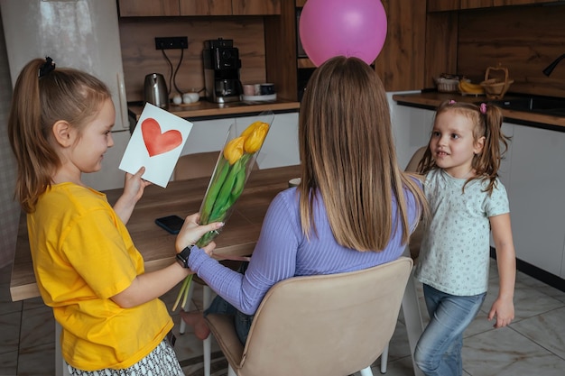 As filhas parabenizam a mãe no Dia das Mães um cartão com flores de coração e um balão