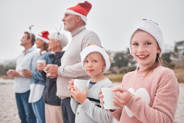 As gerações familiares e o Natal bebem e veem ao ar livre durante as férias e o tempo festivo na praia Pais, avós e filhos felizes com caneca de chocolate quente e chapéu de natal