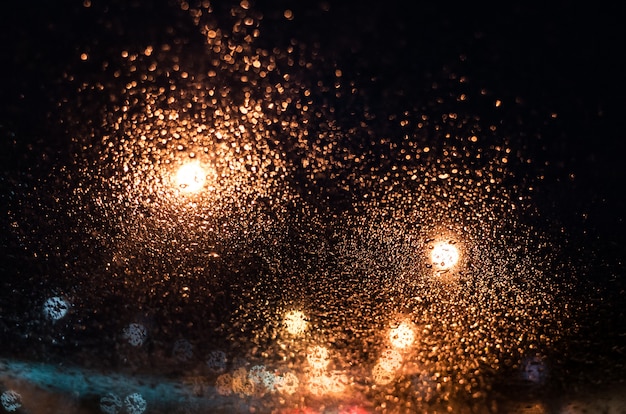 As luzes brilhantes da cidade da noite através do vidro nas gotas de chuva.