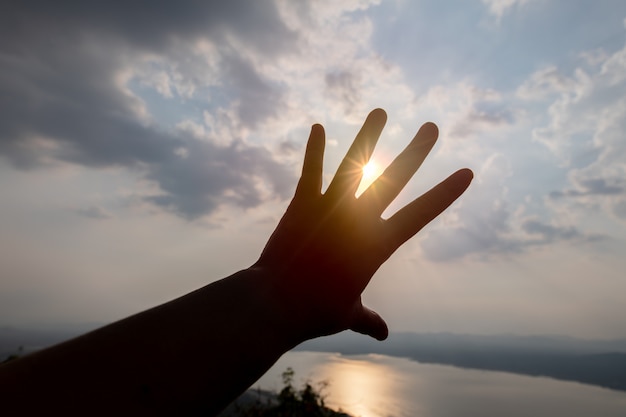 As mãos aparecem na silhueta contra o céu do sol