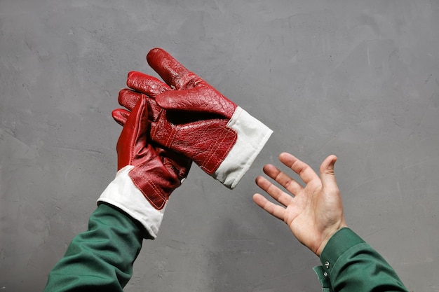 As mãos colocam ou removem a superfície texturizada da luva de trabalho de couro forte fechada sobre fundo cinza