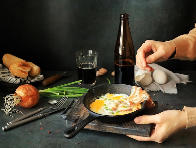 As mãos colocam uma frigideira com ovos mexidos e bacon na mesa com cerveja escura