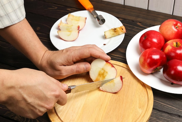 Foto as mãos cortam a suculenta maçã vermelha com a faca na tábua, cozinhando maçãs sem caroço para a sobremesa