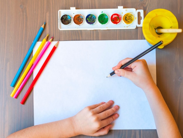 As mãos da criança são pintadas com lápis de cor em uma folha de papel branca