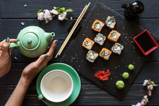 As mãos da garota segurando chá perto de Sushi