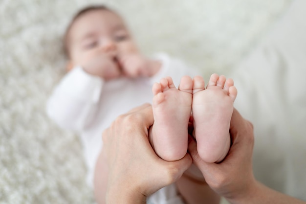 As mãos da mãe seguram as pequenas noites de um bebê recém-nascido em um sofá branco Amor e cuidado materno Os calcanhares do bebê em foco