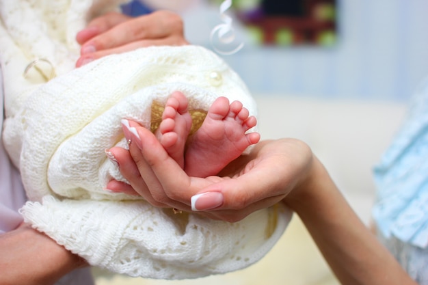 As mãos da mãe seguram as pequenas pernas do bebê recém-nascido, envolto em um cobertor branco e quente
