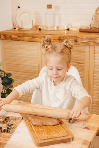 As mãos da menina estendem a massa de gengibre com um rolo na cozinha Menina preparando biscoitos de natal em uma mesa de madeira