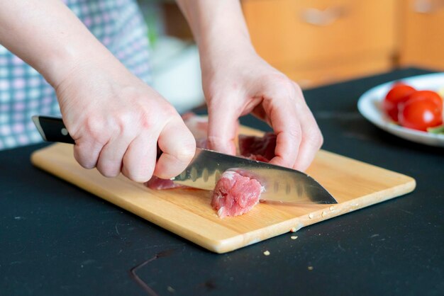 As mãos da mulher cortaram a carne em uma placa de madeira b