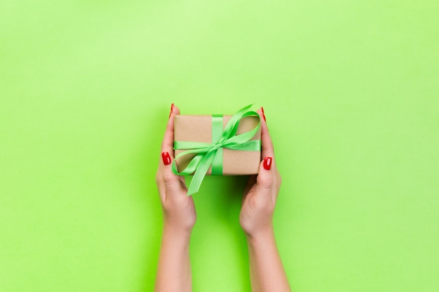 As mãos da mulher dão o Valentim envolvido ou o outro presente feito a mão do feriado no papel com fita verde.