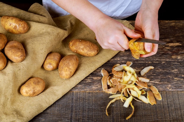 As mãos da mulher descascam as cascas de batata na tábua de corte de madeira três batatas limpas no prato cozinham limpas