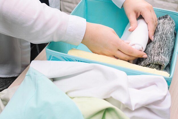 As mãos da mulher dobram suas roupas e as colocam na caixa de armazenamento azul Armazenamento vertical de roupas arrumando o conceito de limpeza do quarto