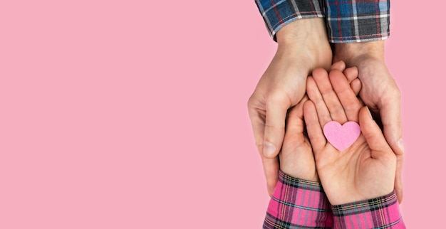 As mãos da mulher e do homem seguram um coração rosa em um fundo rosa O conceito de amor, família e amizade Banner Copie o espaço Vista superior Flatlay Foco seletivo