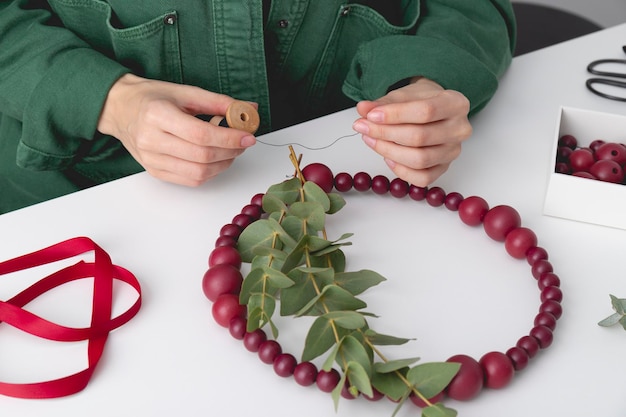 Foto as mãos da mulher estão adicionando o eucalipto com a ajuda de um fio à coroa decorativa festiva