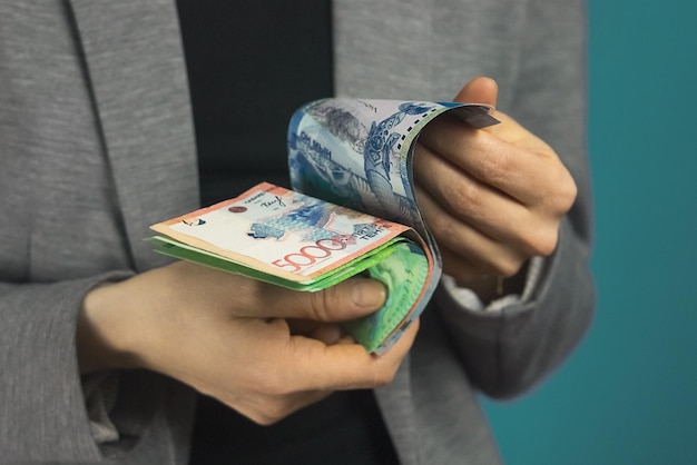 As mãos da mulher guardam a moeda nacional do tenge do Cazaquistão