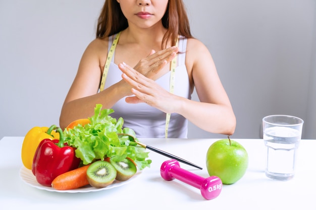 As mãos da mulher infeliz de aisan na camisola interioa que faz um sinal dizem não aos vegatables e às frutas com emoção entediada no tempo de dieta. conceito de comida saudável. fechar-se