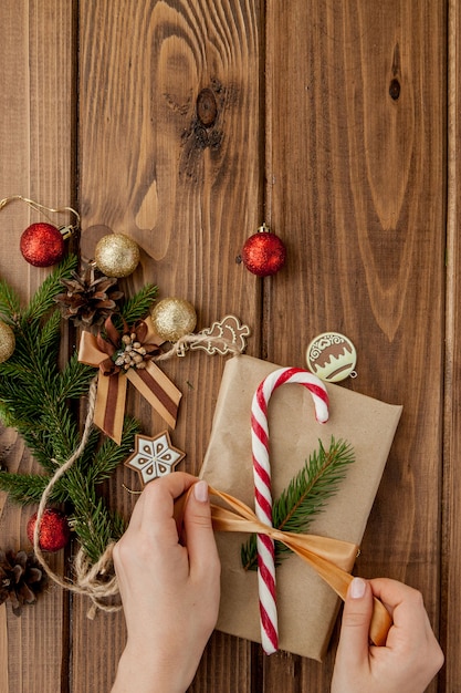 As mãos da mulher que envolvem o presente do Natal, fim acima. Presentes de Natal despreparados em madeira com elementos de decoração e itens, vista superior. Embalagem de Natal ou ano novo DIY.