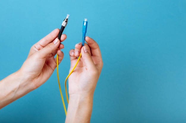 As mãos da mulher seguram o modo único do cabo de remendo da fibra óptica do conector sc e fc no fundo azul.