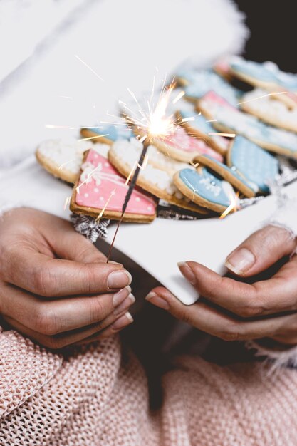 Foto as mãos da mulher seguram um prato branco com biscoitos de natal de inverno decorados e um brilho