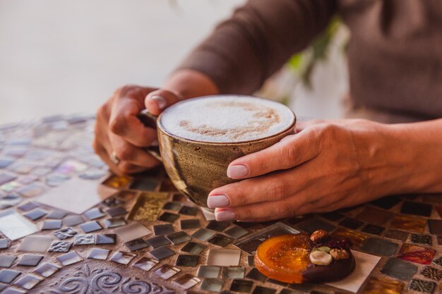 Foto as mãos da mulher seguram uma xícara de café cappuccino em uma mesa de vidro colorida no café