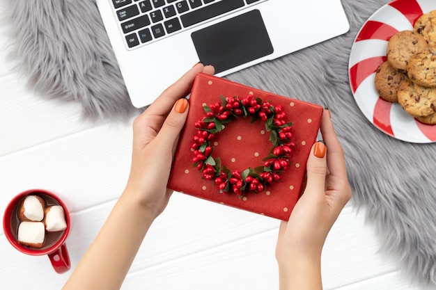 As mãos da mulher segurando um presente com chocolate e biscoitos em fundo peludo. Compras online de Natal trabalhando a partir do conceito de casa.