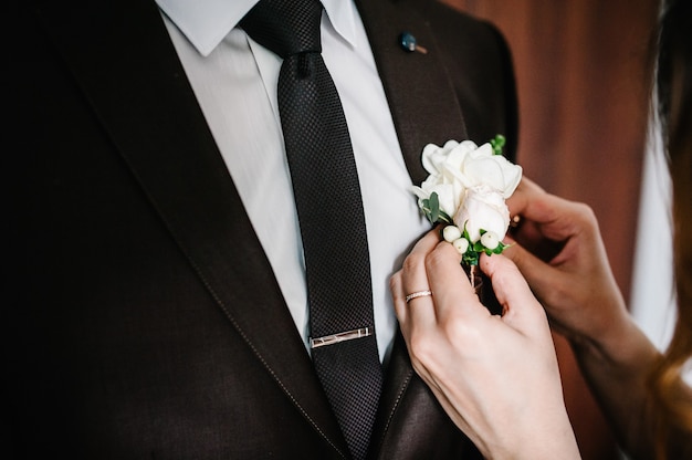 As mãos da noiva colocam o noivo na jaqueta de uma flor na lapela de casamento. Conceito de casamento.