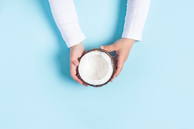 As mãos das crianças estão segurando a metade de um coco em um fundo azul.