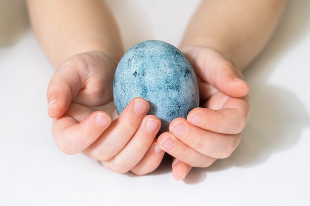 As mãos das crianças estão segurando um ovo de Páscoa. Lindo ovo pintado para a Páscoa. Close-up de um ovo azul