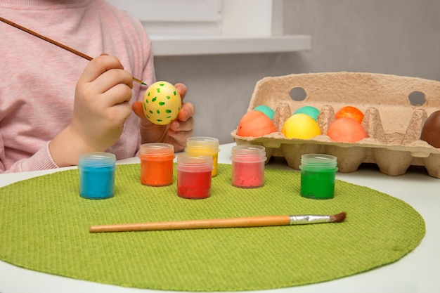 As mãos das crianças pintam com tintas e ovos de Páscoa e as colocam em um recipiente
