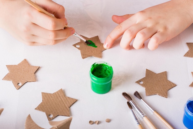 As mãos das crianças pintam uma estrela de papelão para decorações artesanais de Natal diy