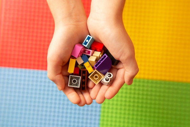 Foto as mãos das crianças seguram detalhes coloridos do construtor de lego em um fundo de plataformas