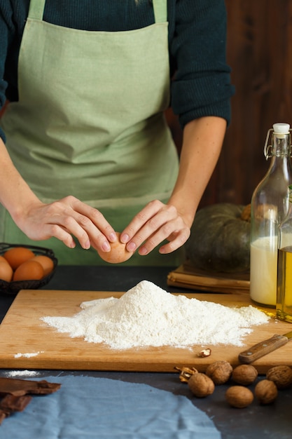 As mãos das mulheres amassam a massa. O confeiteiro está dirigindo um ovo para a farinha. Na mesa de madeira estão os ingredientes de panificação.