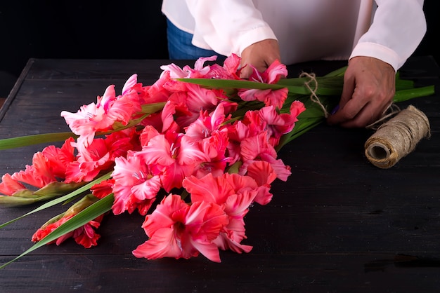 As mãos das mulheres criam um buquê de flores de gladíolo