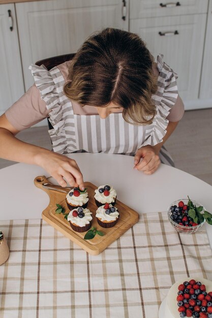 As mãos das mulheres decoram muffins com mirtilos frescos e framboesas e folhas de hortelã.