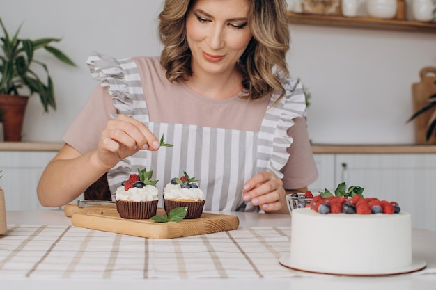 As mãos das mulheres decoram muffins com mirtilos frescos e framboesas e folhas de hortelã.