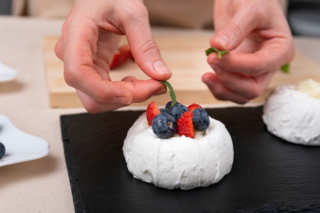 As mãos das mulheres decoram o bolo. frutas frescas e merengue branco.