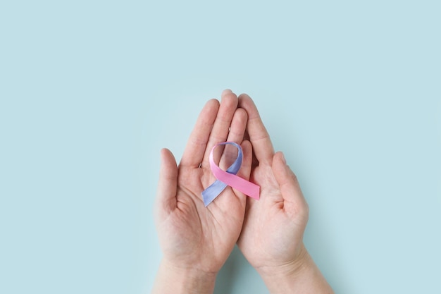 As mãos das mulheres do dia mundial da tireóide seguram a fita de conscientização do câncer de tireóide em teal pink blue