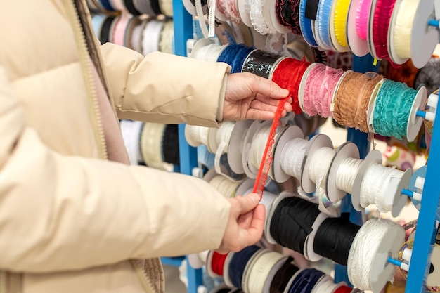 As mãos das mulheres escolhem uma fita vermelha de fitas multicoloridas em uma loja de artesanato