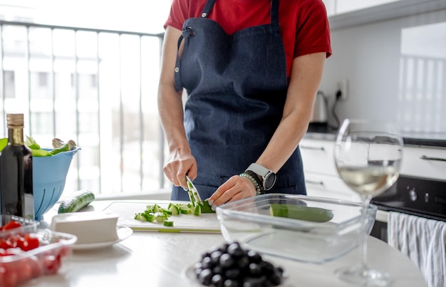 As mãos das mulheres estão cortando pepino para salada grega com um copo de vinho branco nas proximidades